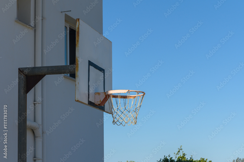 Naklejka premium Urban basketball hoop under a clear blue sky in a sunny afternoon.