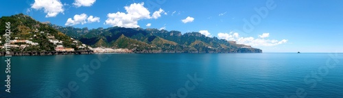 A panoramic view of serene blue waters bordered by lush green mountains under a clear blue sky.