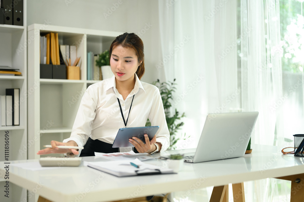 Focused female accountant calculating data and using digital tablet in a office Focused female accountant calculating data and using digital tablet in a office