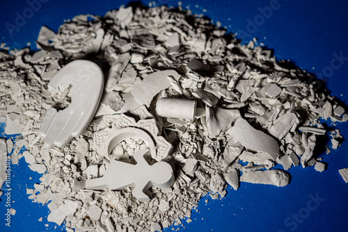 A pile of broken white ceramic fragments, including a hand, a gear, a figurine, and other shapes, scattered over a blue surface. photo