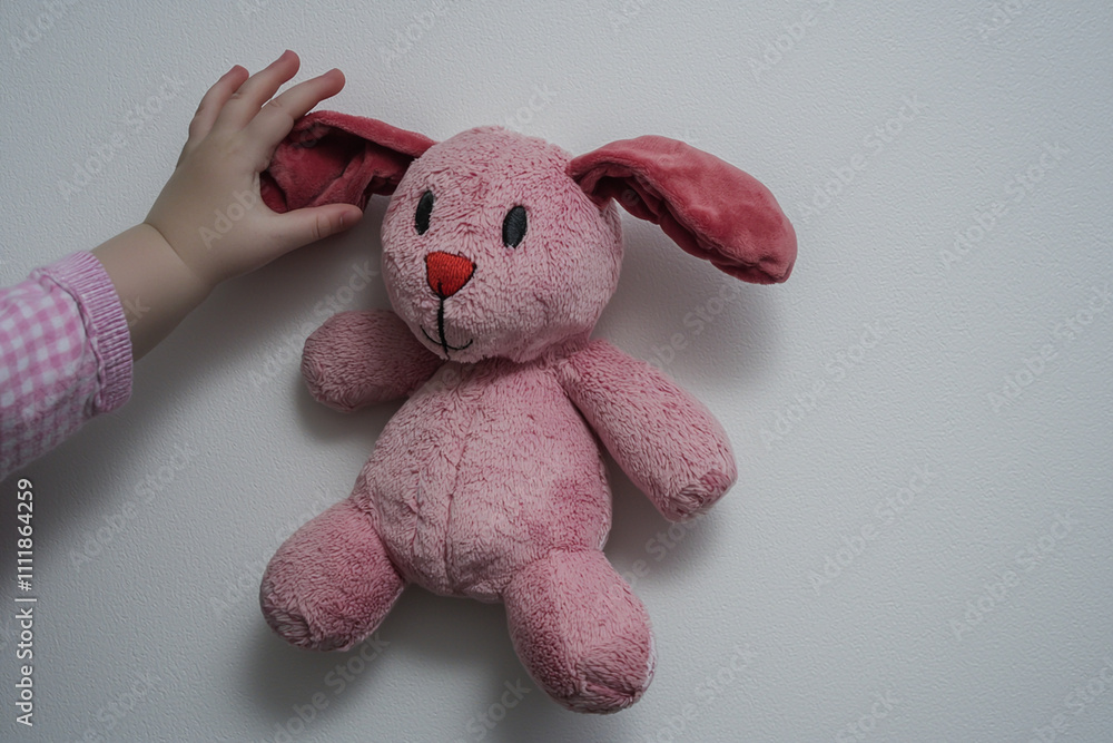 Soft pink bunny toy held by a child's hand against a wall Soft pink bunny toy held by a child's hand against a wall