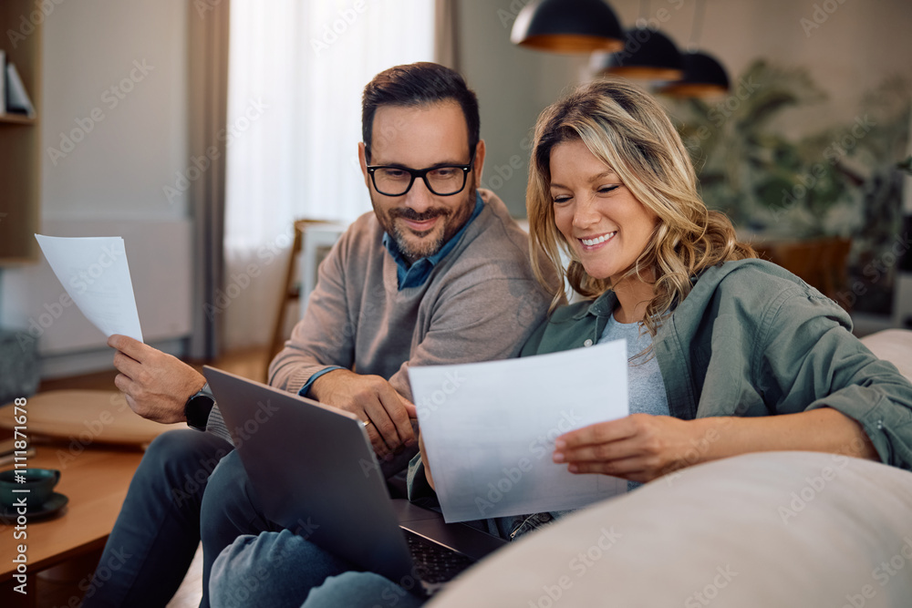 Happy couple analyzing paperwork while using laptop at home.