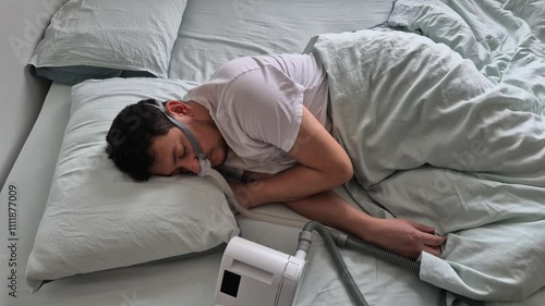 A man in his mid-thirties with sleep apnea sleeps using a nasal mask and CPAP device in a bed in his house