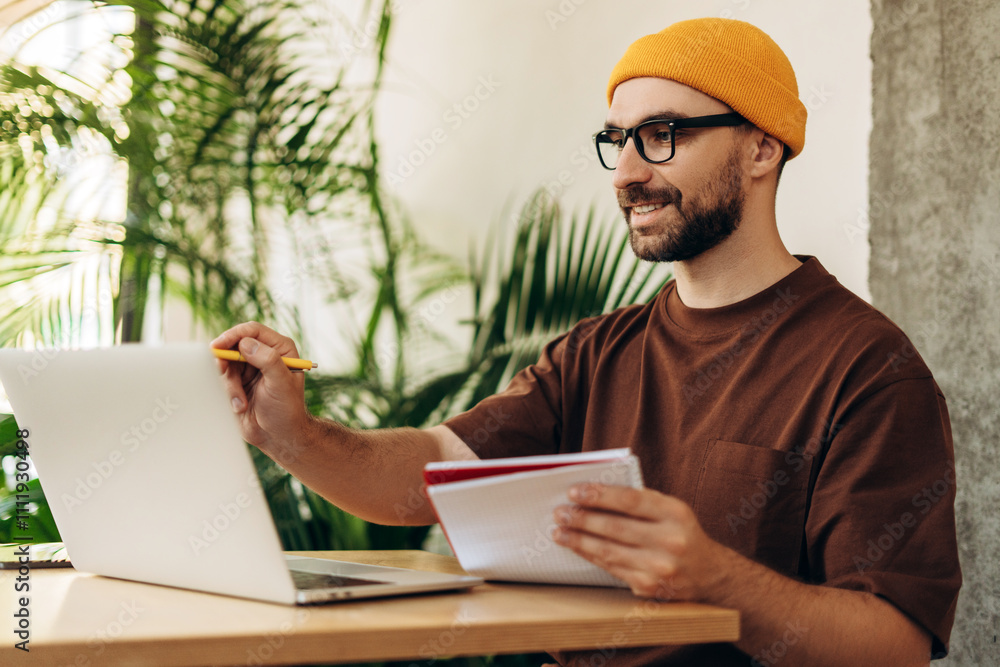 © Maria Vitkovska - Happy successful man, student wearing stylish yellow hat and eyeglasses taking notes, using laptop © Maria Vitkovska - Happy successful man, student wearing stylish yellow hat and eyeglasses taking notes, using laptop
