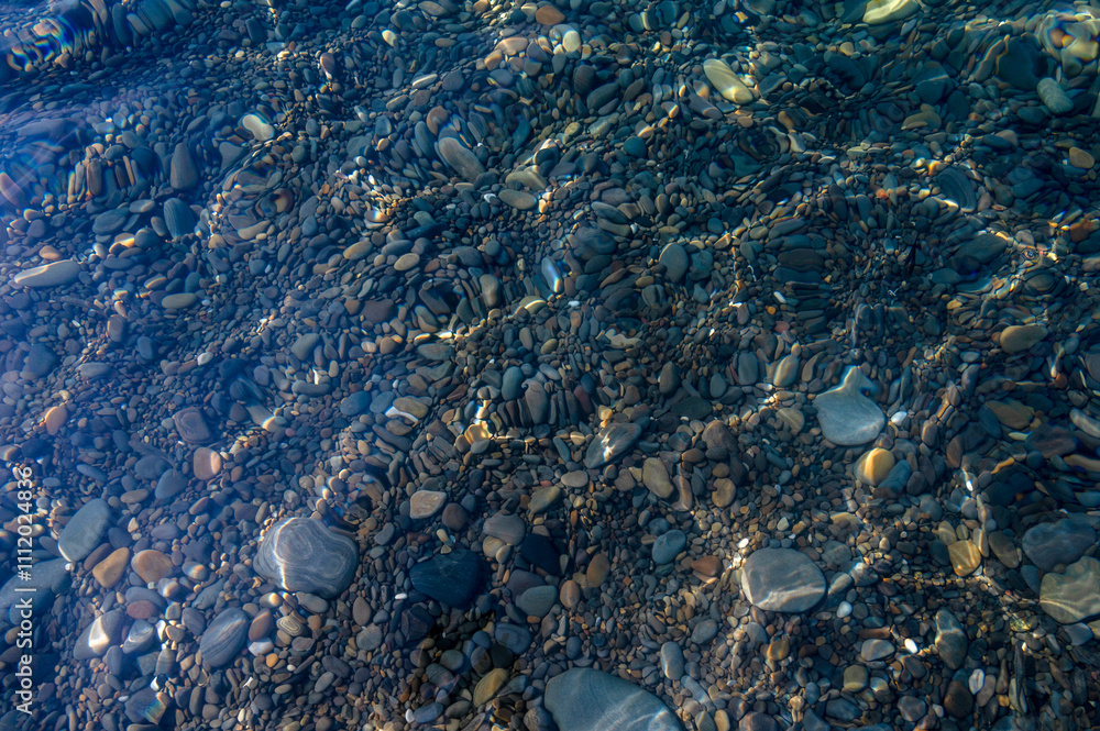 Underwater pebble backgrounds. Colorful stones sea bottom in the sun rays. View from above through clear water. Seascape wallpaper texture. Defocus. Underwater pebble backgrounds. Colorful stones sea bottom in the sun rays. View from above through clear water. Seascape wallpaper texture. Defocus.