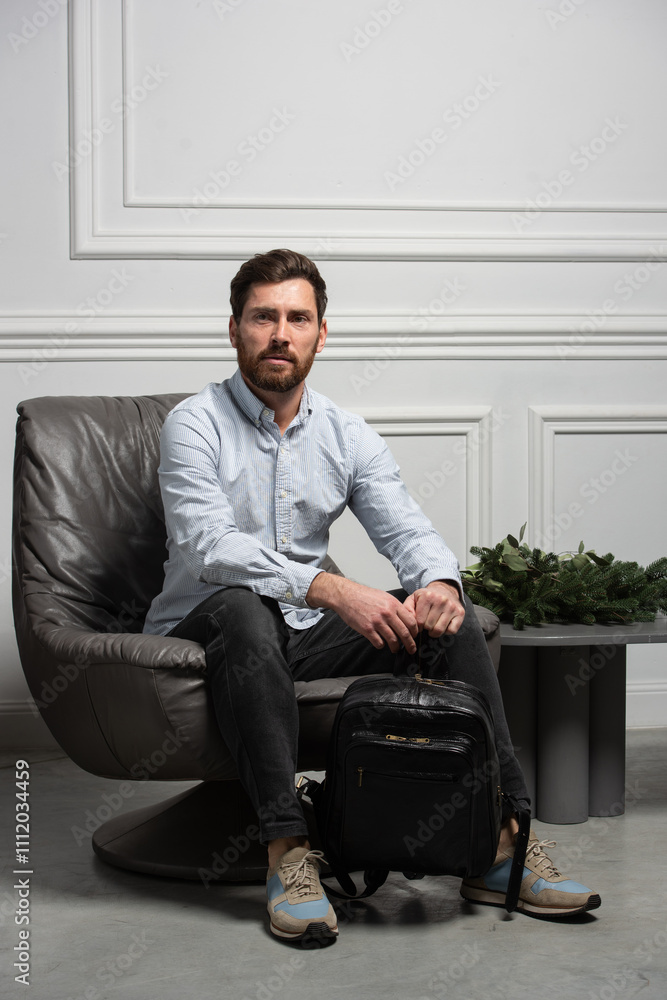 Fototapeta premium A man is comfortably sitting in a chair, resting with a backpack near him