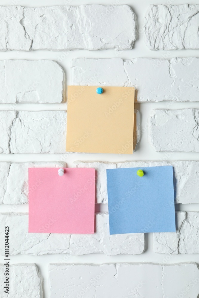 Colored paper stickers attached with pushpin on a white brick wall Colored paper stickers attached with pushpin on a white brick wall