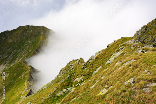 clouds in the mountains. outdoor adventure landscape of transylvania alps on a sunny summer day. scenery with steep rocky slopes with grass. beautiful nature background. explore fagaras