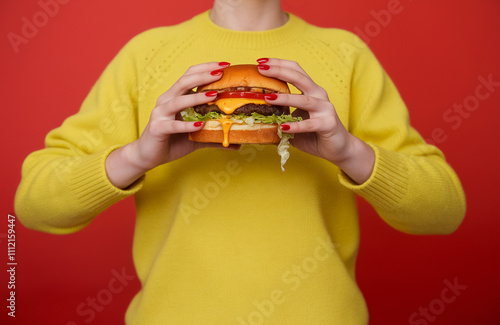 A person wearing a bright yellow sweater. holding a burger with juicy meat patty, lettuce, and a dripping sauce photo