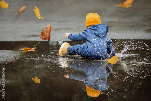 Obraz na plátně Happy toddler walks through the puddles in blue jumpsuit with splashes close-up and copy space