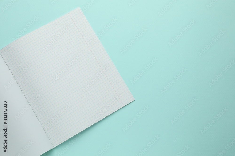 Open copybook with checkered sheets of paper on light blue background, top view. School stationery Open copybook with checkered sheets of paper on light blue background, top view. School stationery
