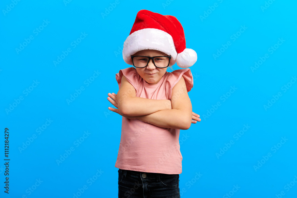 Obraz premium Upset little girl in a Santa hat holds a beautifully wrapped gift, her expression capturing the bittersweet emotions of the holiday season. Set against a striking blue background...