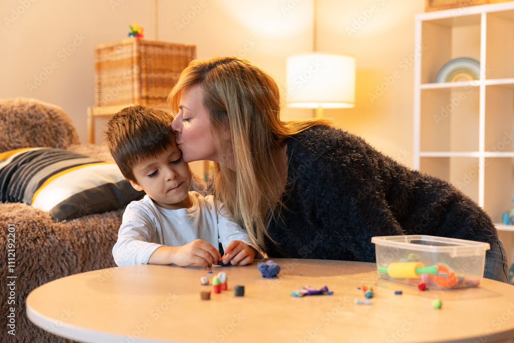 Fototapeta premium Loving mother kissing her son while playing with clay at home