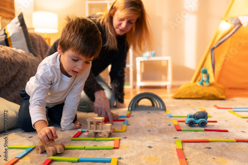 Child playing with wooden toys and building road with colorful planks, mother helping