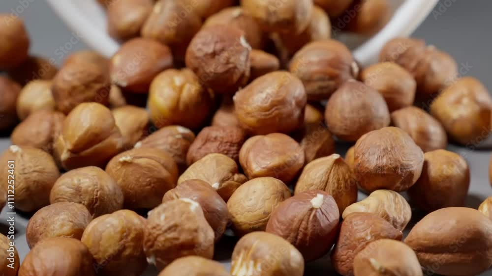 Falling hazelnuts on grey background. Hazelnuts fall on table. Close-up of brown nuts falling from white bowl on gray table. Pile of healthy food for vegan. Slow motion Falling hazelnuts on grey background. Hazelnuts fall on table. Close-up of brown nuts falling from white bowl on gray table. Pile of healthy food for vegan. Slow motion