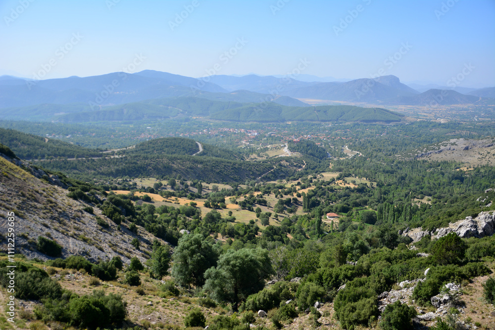 a view of a valley and some green trees and mountains in the background a view of a valley and some green trees and mountains in the background