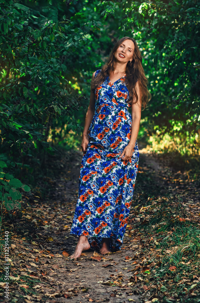 Joyful woman with long hair walks barefoot along forest path. She holds long dress in hands and laughs. Joyful woman with long hair walks barefoot along forest path. She holds long dress in hands and laughs.