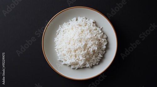 A simple, white bowl filled with fluffy, cooked rice, set against a dark background, highlighting the texture and color of the rice.