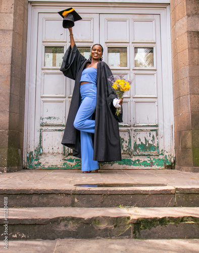 A you black woman wearing a graduation gown looking excited to be a graduand