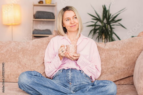Adult woman sitting on the sofa at home and having a cup of coffee