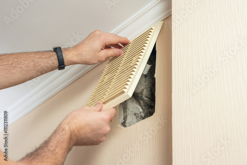 A man removes a plastic ventilation grille for later cleaning