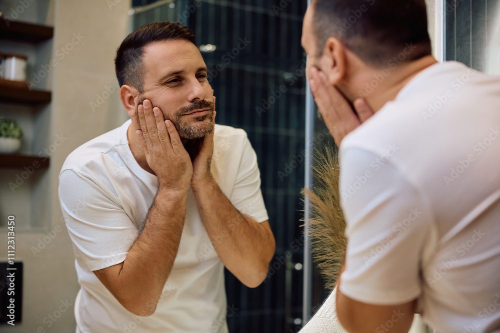Obraz premium Reflection in mirror of mid adult man looking at his face.