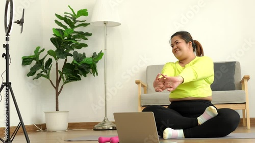 Asian overweight woman doing stretching exercise at home on fitness mat. Home activity training, online fitness class. Stretching training workout on yoga mat at home for good health and body shape.