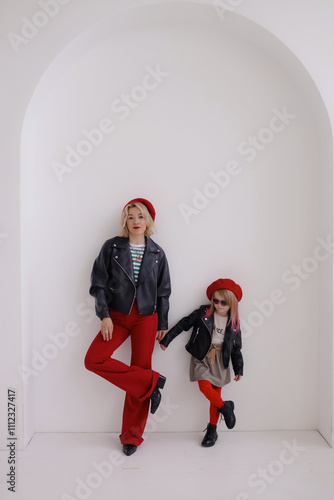 A woman and a girl are standing against the wall, holding hands.