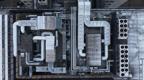 Aerial view of an industrial rooftop showcasing HVAC systems, vents, and piping, with snow covering parts of the surface in a winter setting.