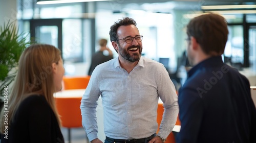 A man laughing and chatting with colleagues in a lively office space, exuding a fun and supportive work environment.