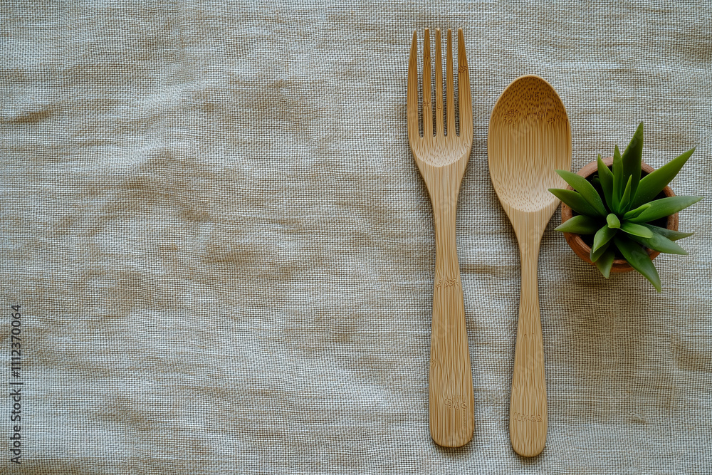 A simple table setting featuring bamboo utensils and a small succulent in a pot on a neutral fabric background A simple table setting featuring bamboo utensils and a small succulent in a pot on a neutral fabric background