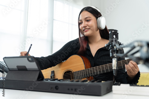 Professional Women Musician composing a song with acoustic guitar, piano keyboard and condenser microphone. She mixing and mastering her song with table at digital recording home studio. photo