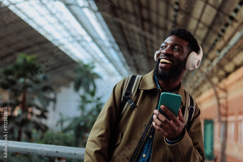 Fotografía Tourist listening to music on his smart phone and smiling at the station