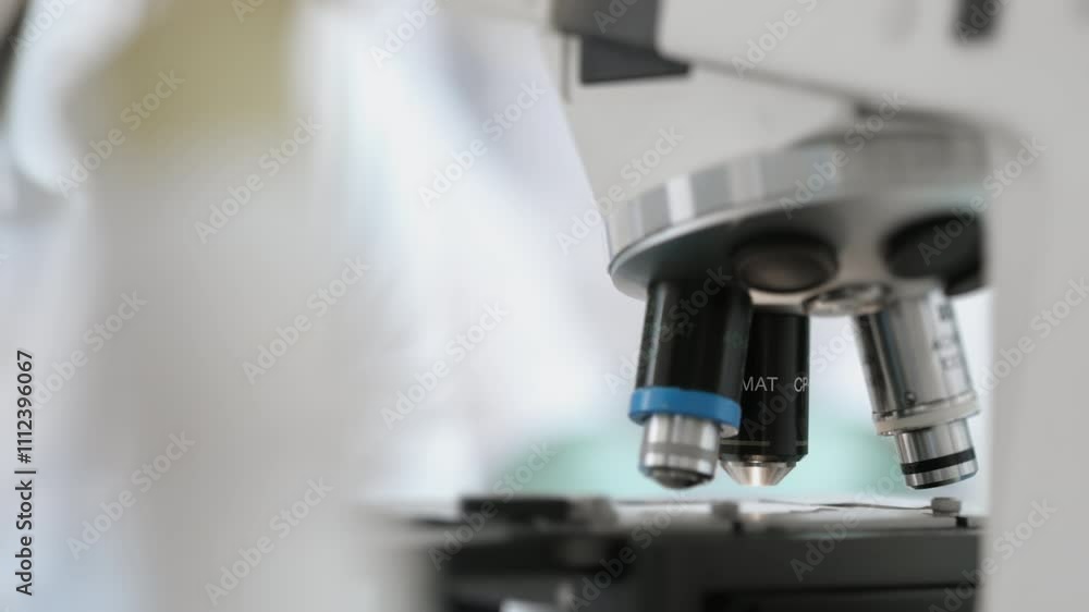 A medical laboratory worker places a glass with a sample under a microscope and adjusts the microscope lenses. Modern scientific laboratory. Research equipment for the laboratory. A medical laboratory worker places a glass with a sample under a microscope and adjusts the microscope lenses. Modern scientific laboratory. Research equipment for the laboratory.