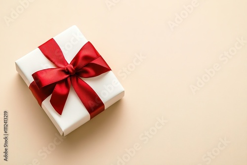 White gift with red ribbon on beige background, top view.