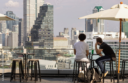 Obraz na płótnie wo men tourists while relaxing looking at Modern skyscrapers of Bangkok city. w salonie