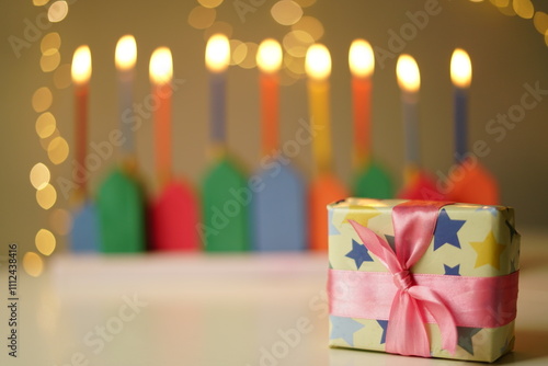 DIY Wooden Hanukkiah with Colorful Candles. High quality photo. The lit candles create a cozy and festive atmosphere with a gift, with lots of lights in the background This handmade menorah beautifull photo