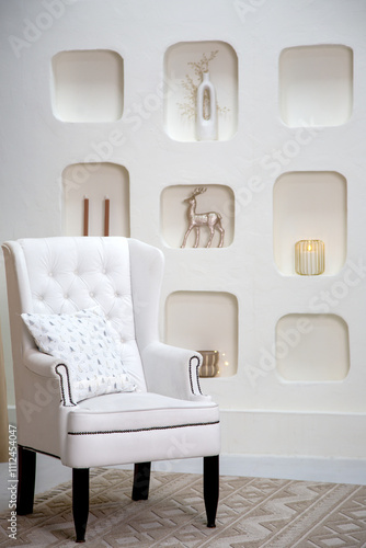 Modern minimalist interior featuring a white tufted armchair with a decorative pillow, set against a wall with built-in niches showcasing elegant holiday decor