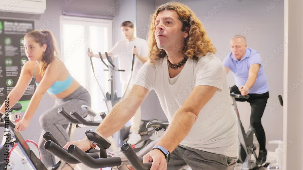 Focused sporty adult man working out on stationary bicycle in gym. Physical activity and fitness concept Focused sporty adult man working out on stationary bicycle in gym. Physical activity and fitness concept
