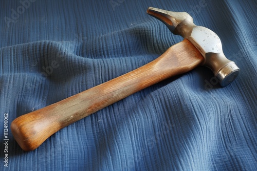 An old hammer with a polished wooden handle and a slightly tarnished metal head, displayed on a blue linen fabric background for a soft, vintage look. 32k, full ultra hd, high resolution - photo