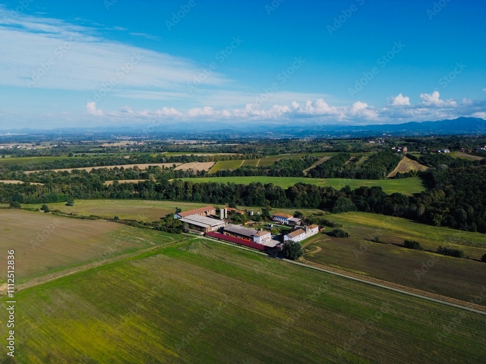 Expansive aerial view of rustic farmhouse surrounded by lush fields and distant mountains during clear day Expansive aerial view of rustic farmhouse surrounded by lush fields and distant mountains during clear day