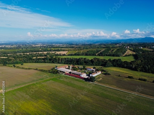 Expansive aerial view of rustic farmhouse surrounded by lush fields and distant mountains during clear day