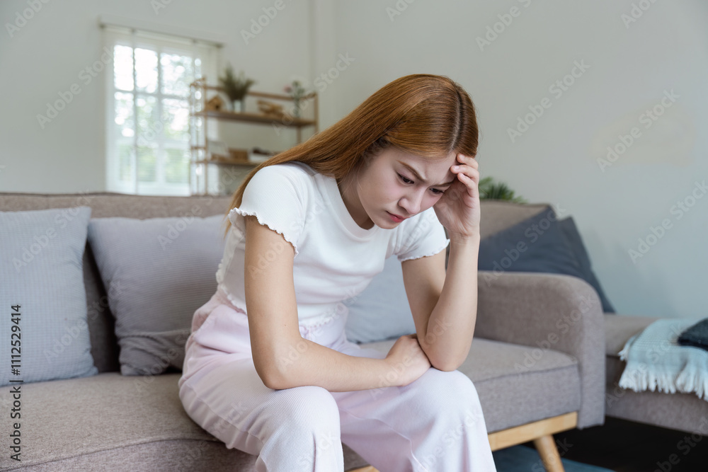 Young Woman Feeling Unwell at Home Sitting on Couch in Living Room with Hand on Forehead Young Woman Feeling Unwell at Home Sitting on Couch in Living Room with Hand on Forehead