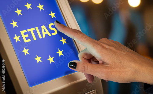 Close-up of a hand pointing at a touchscreen displaying the ETIAS logo with EU stars, symbolizing the European Travel Information and Authorization System process photo