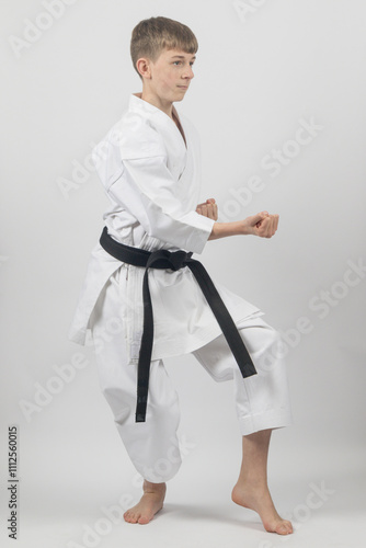 Fifteen year old male teenage karate black belt in a cat stance punching, studio shot against a white background photo