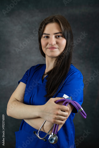 beautiful female doctor or medical student  in blue uiform with stethoscope against dark background photo