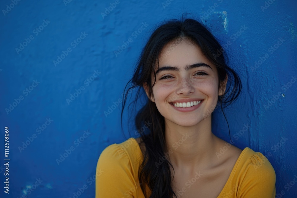 A smiling woman with long black hair standing in front of a blue wall A smiling woman with long black hair standing in front of a blue wall