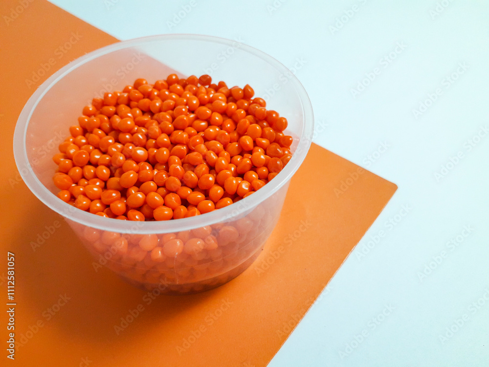 Orange masterbatch granules in plastic cup on white and orange background,color pigment carrier polymer in plastic industry.Suitable for plastic company catalog design Orange masterbatch granules in plastic cup on white and orange background,color pigment carrier polymer in plastic industry.Suitable for plastic company catalog design