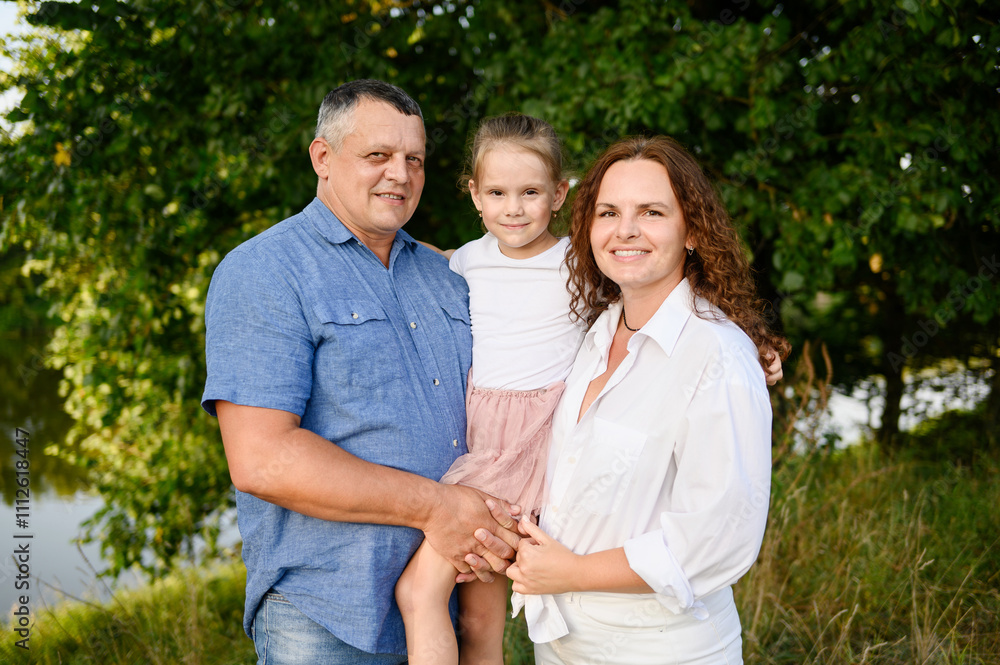 Middle aged parents holding daughter in arms enjoying time together smiling happily during outdoor recreation in park. Happy family concept, vacation, family values. International Day of Families Middle aged parents holding daughter in arms enjoying time together smiling happily during outdoor recreation in park. Happy family concept, vacation, family values. International Day of Families