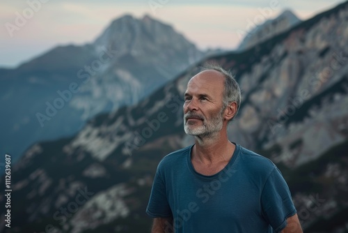 Portrait of a blissful man in his 50s dressed in a casual t-shirt in front of backdrop of mountain peaks